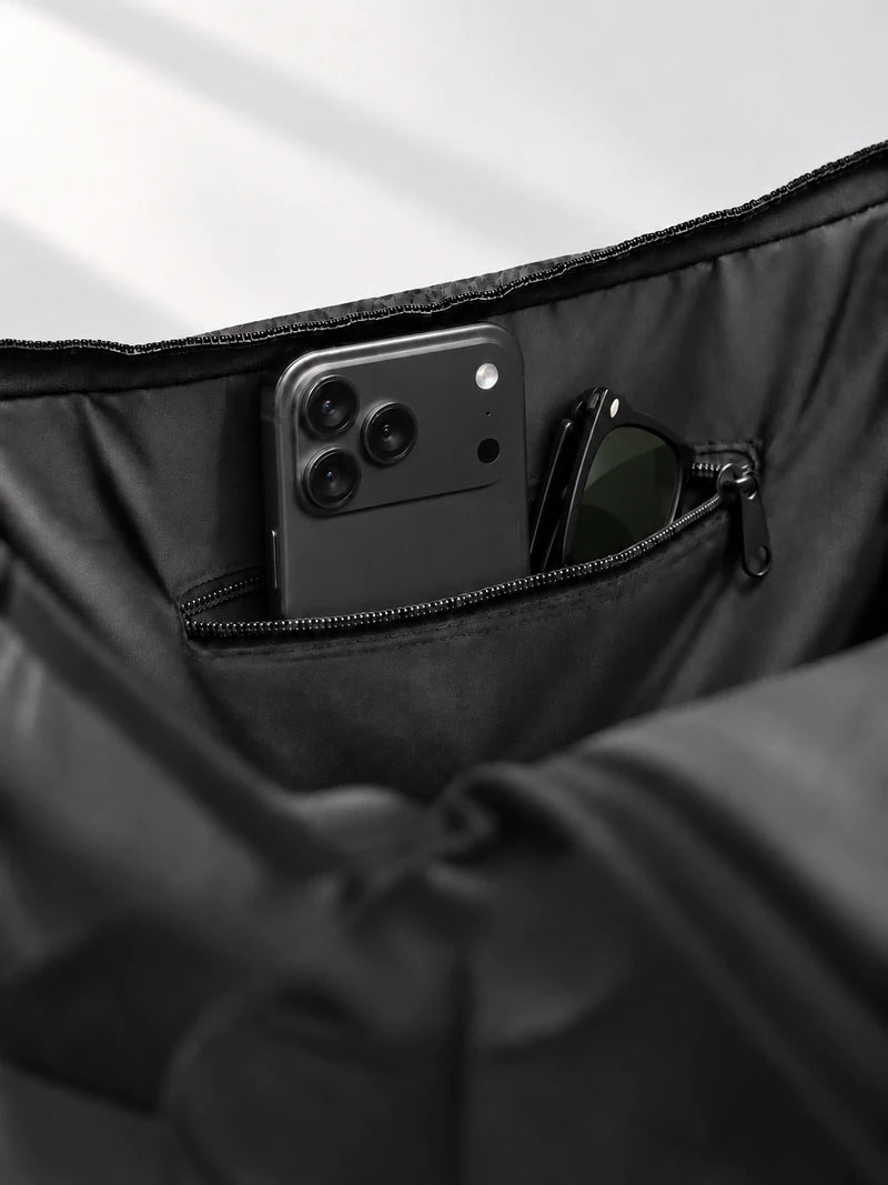 Poche intérieure zippée contenant un téléphone et des lunettes de soleil, à l’intérieur du sac CISTA noir.